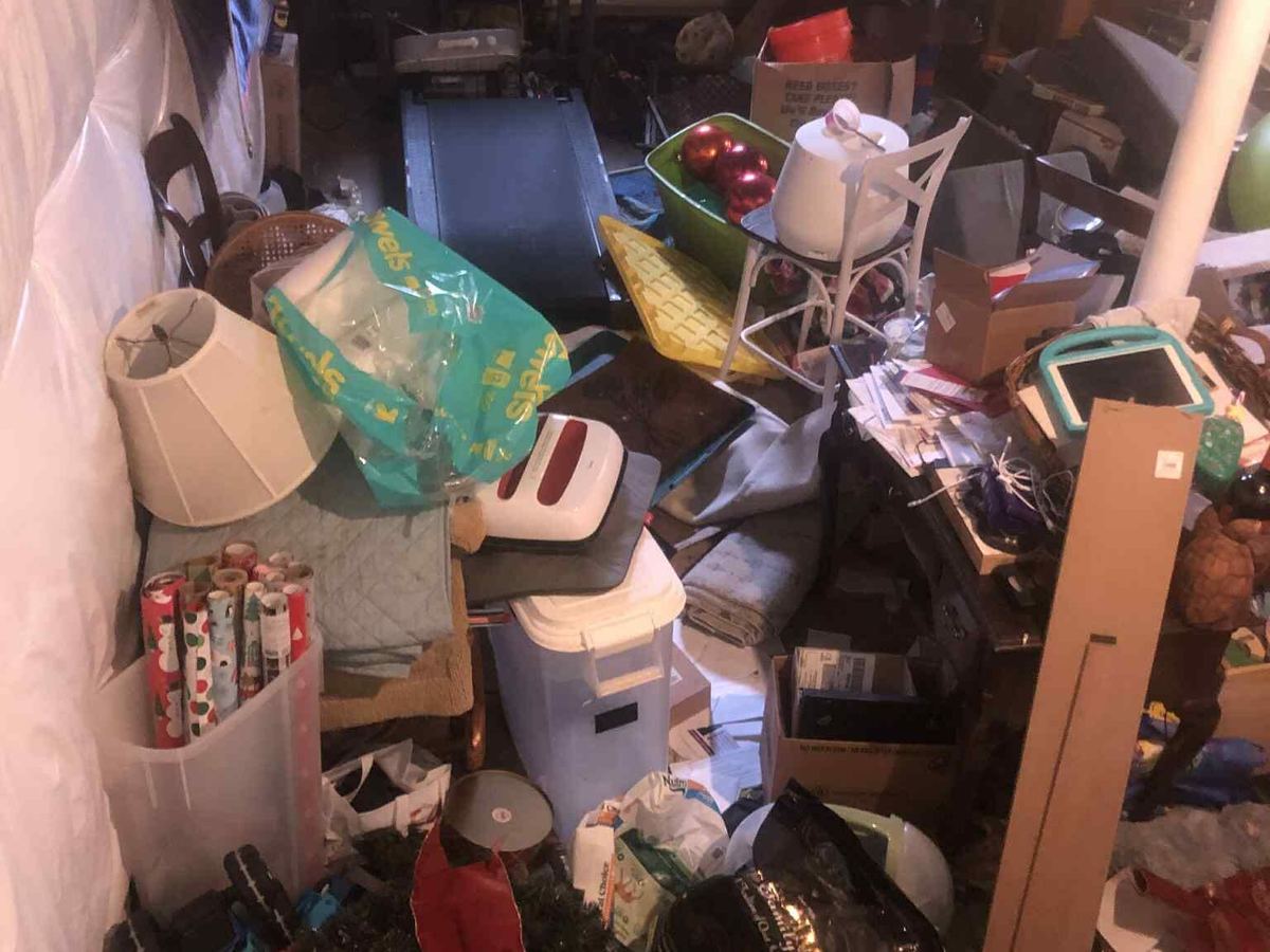 A basement storage room packed with a treadmill, boxes, bags, holiday decorations and old furniture
